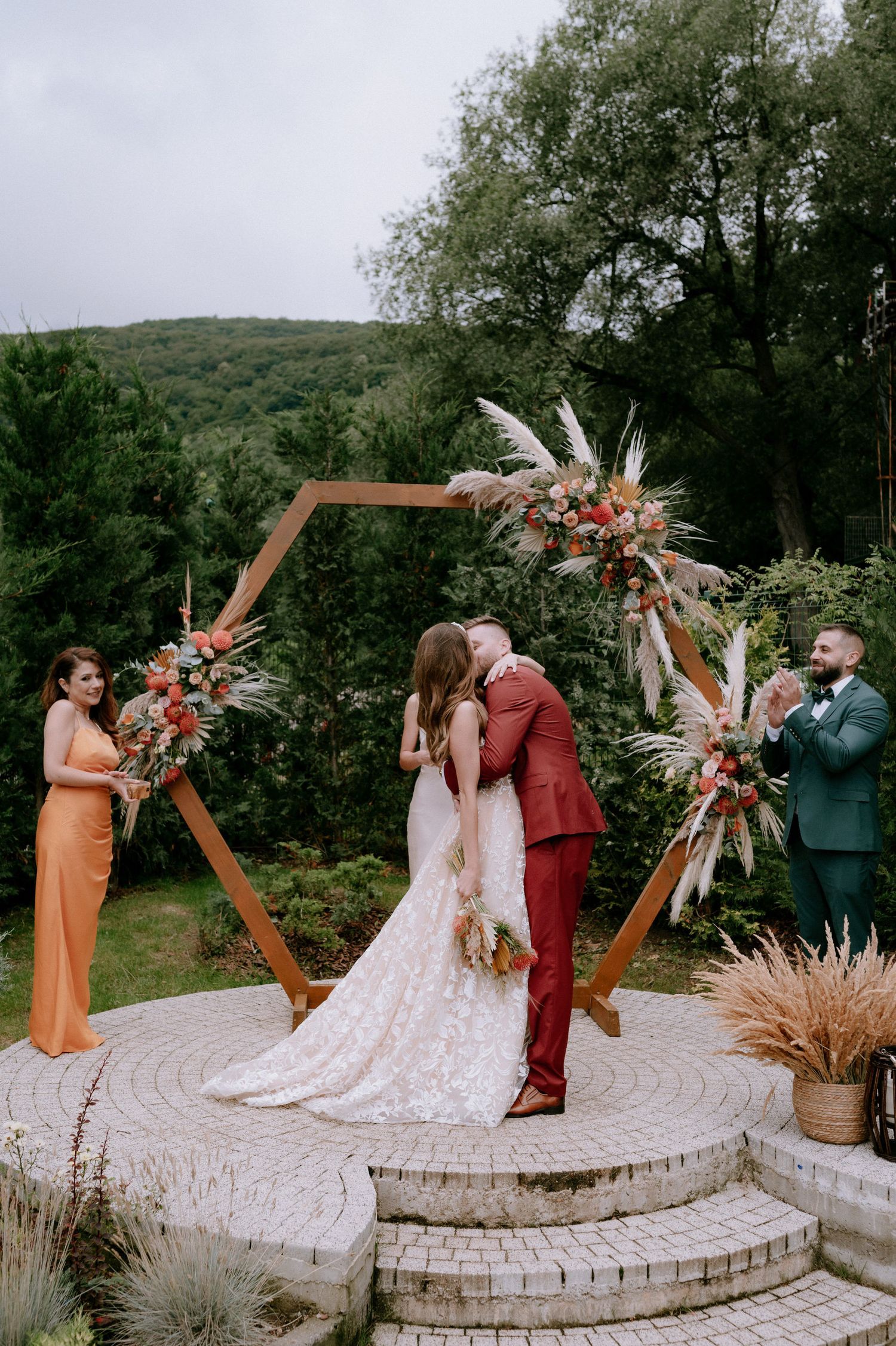 A wedding ceremony setup with a hexagonal wooden arch decorated with dried pampas grass and florals on a stone platform.