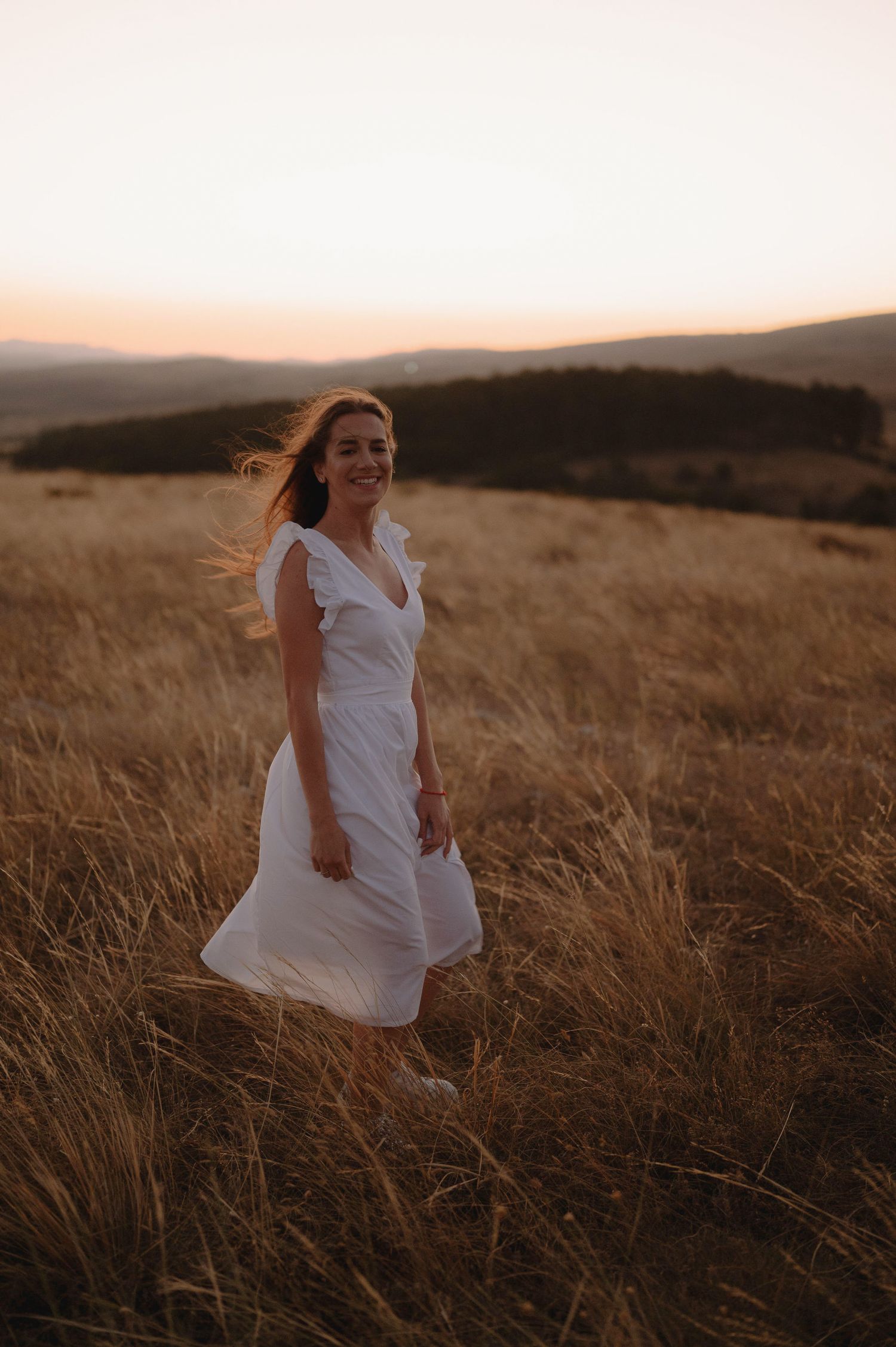 A figure in a flowing white dress runs through golden wheat fields at sunset in a dreamy outdoor setting.