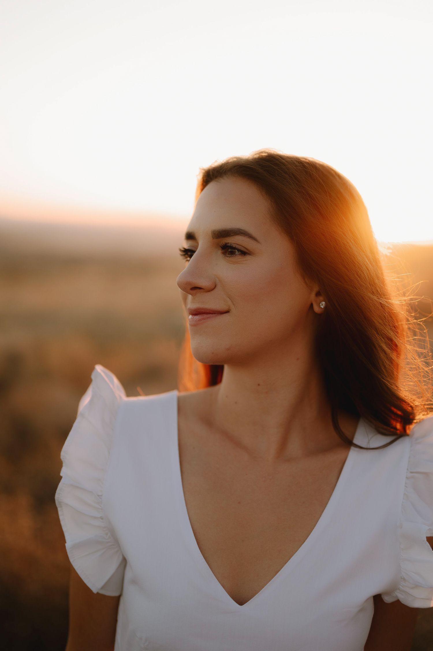 A woman in a white top poses against a warm sunset backdrop with glowing golden light.