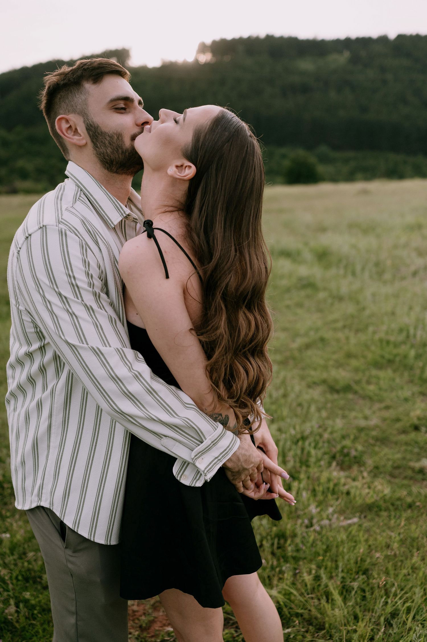 A romantic couple embraces in a grassy meadow at sunset, creating a series of intimate poses against nature's backdrop.