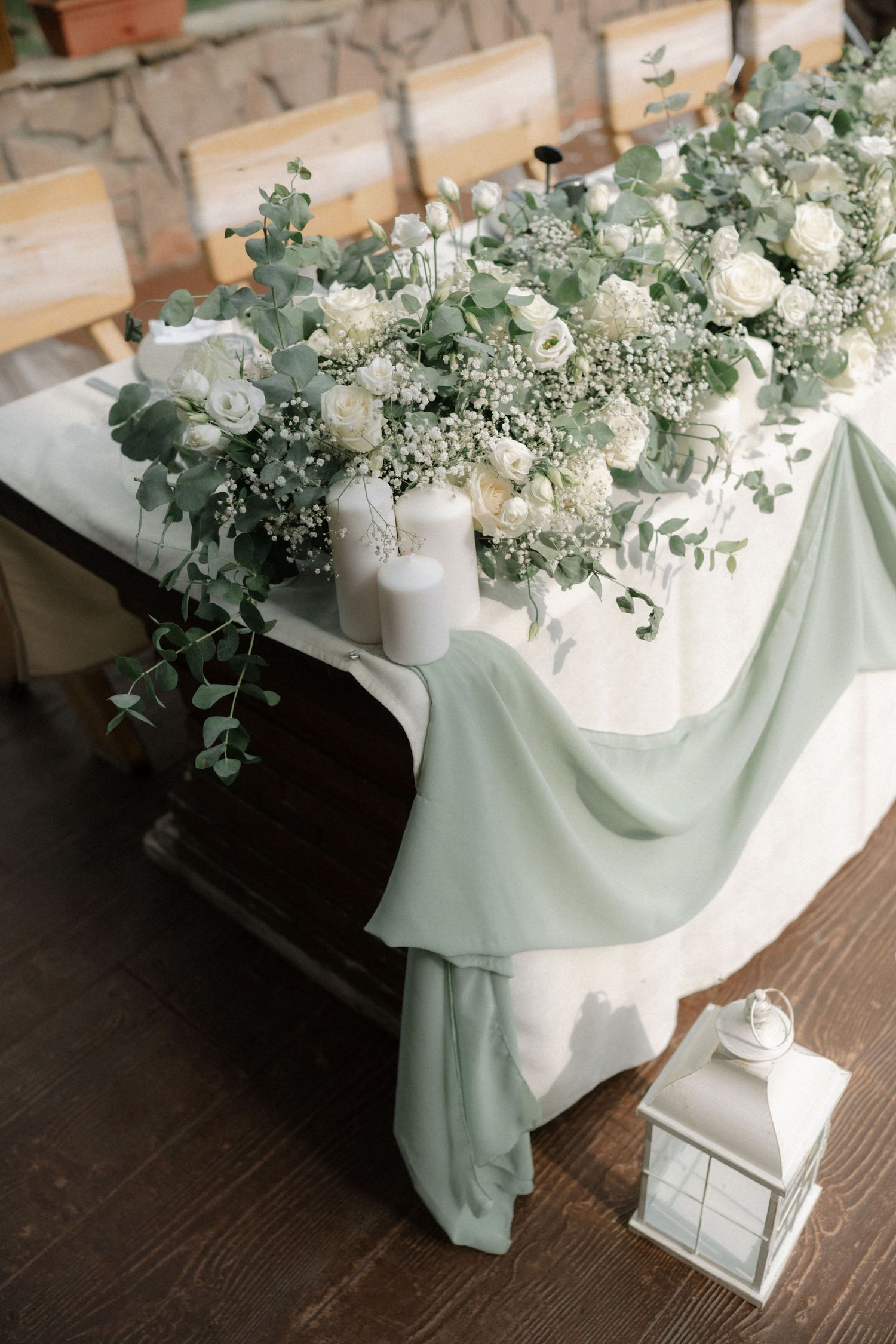 Elegant white floral centerpiece with eucalyptus on dark wooden table with soft mint green fabric draping.