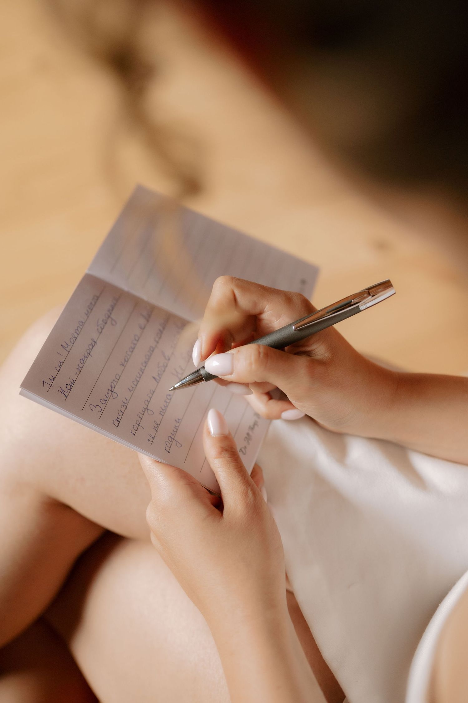Close-up shot of hands writing on a piece of paper with a pen in warm lighting.