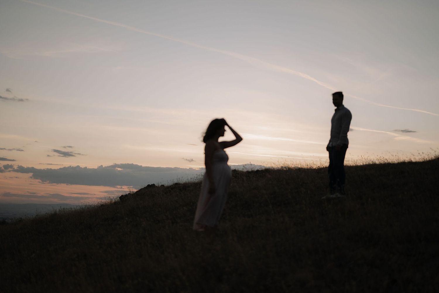 Silhouettes of people standing on a hilltop against a dramatic sunset sky with clouds in the distance.
