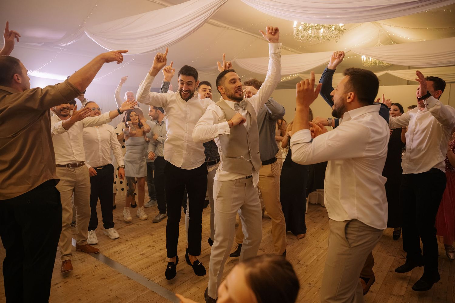 Guests celebrate and dance joyfully at an elegant wedding reception in a decorated banquet hall.
