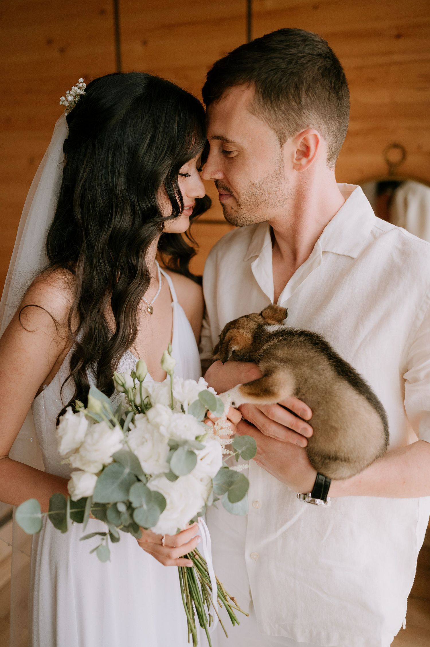 A romantic wedding couple shares an intimate moment while holding a small pet bunny and white floral bouquet.