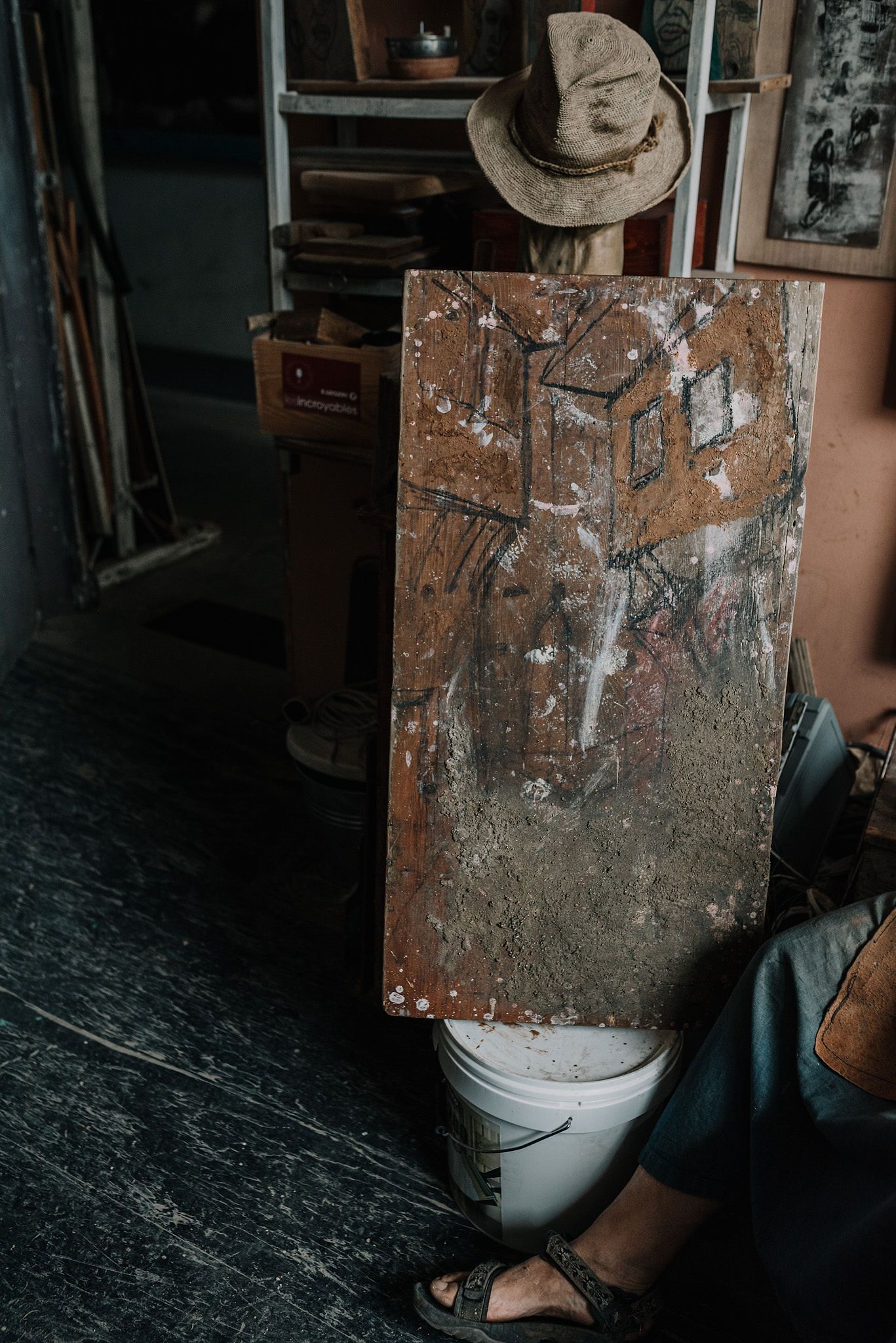 Distressed wooden board with paint marks sits in a dark workshop environment.