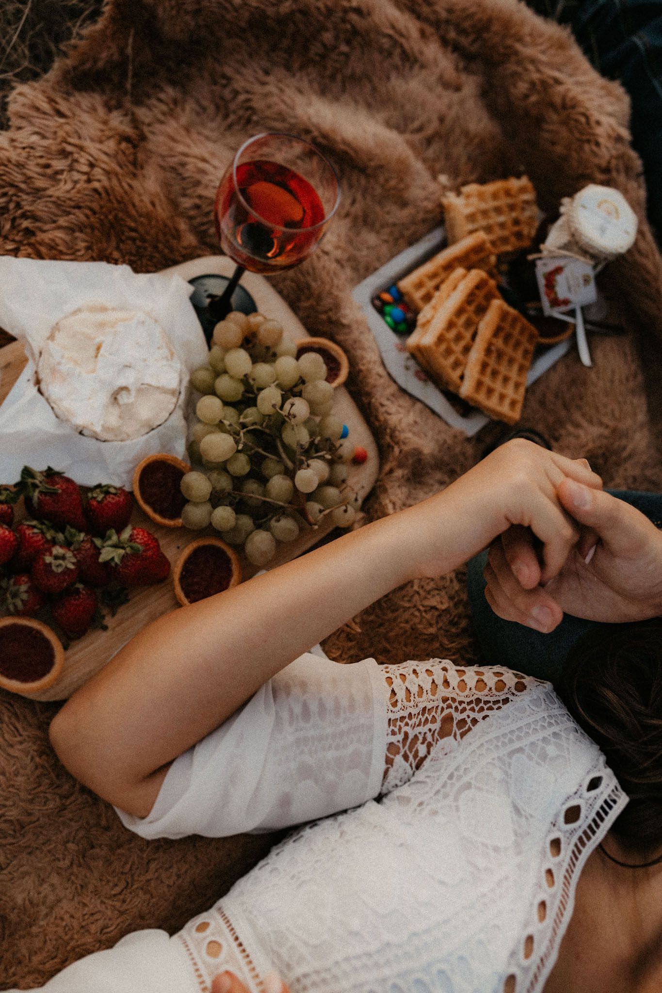 Close-up of picnic spread with grapes, wine, and snacks on a brown blanket.