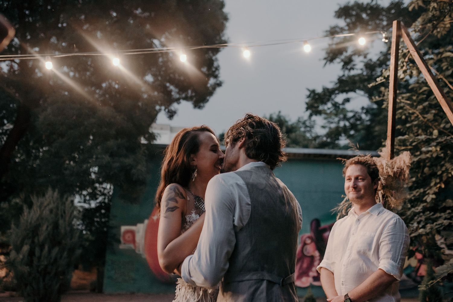 A romantic outdoor evening wedding celebration under string lights with a couple sharing a tender moment.