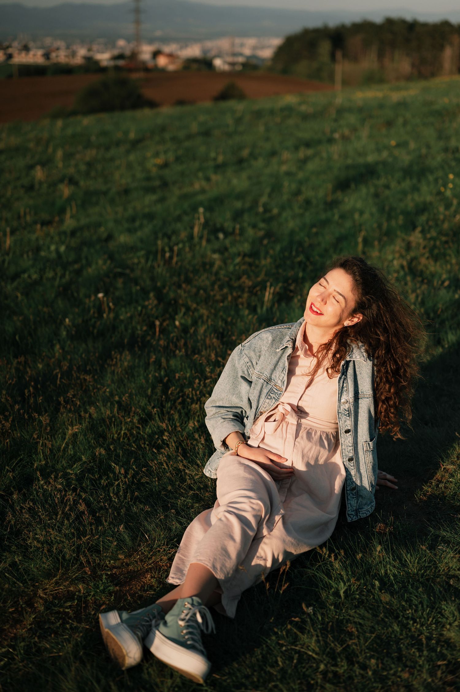 A person in a light colored outfit lies playfully in a green grassy field during golden hour.