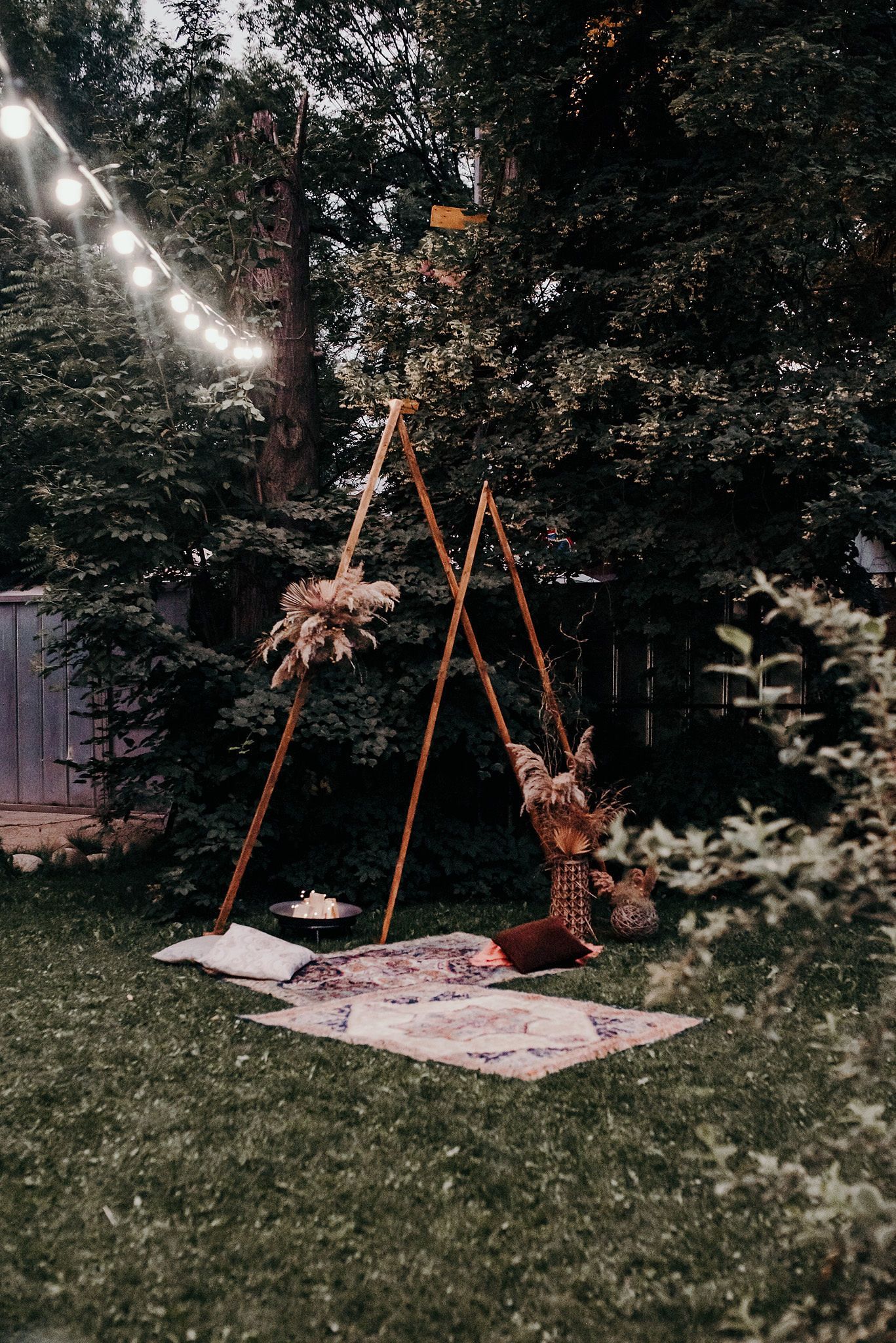 Cozy outdoor setup with string lights and wooden ladder creating a romantic backyard movie viewing area on blankets.