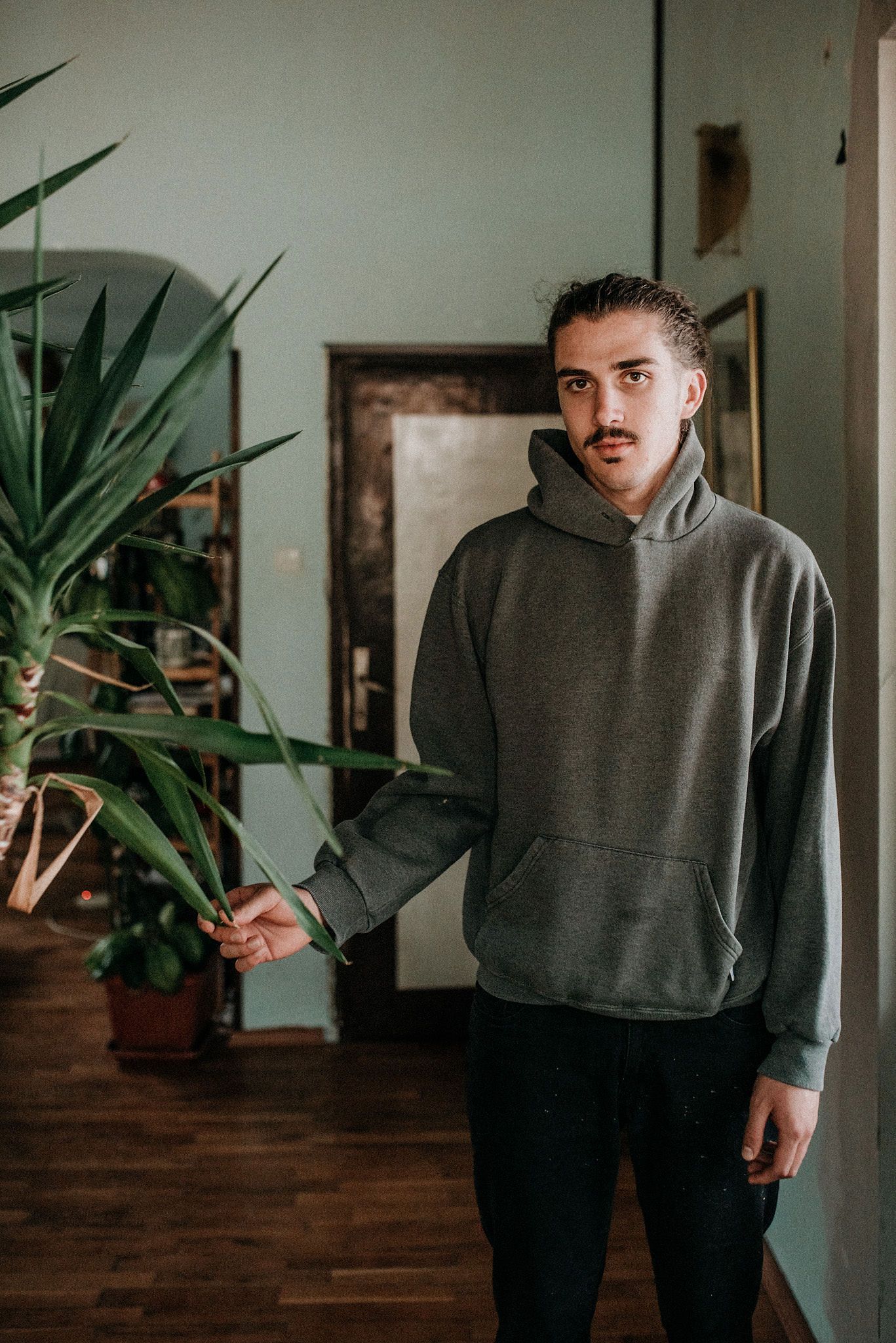 A sequence of poses showing someone in a gray sweatshirt gesturing expressively against a wall with indoor plants.