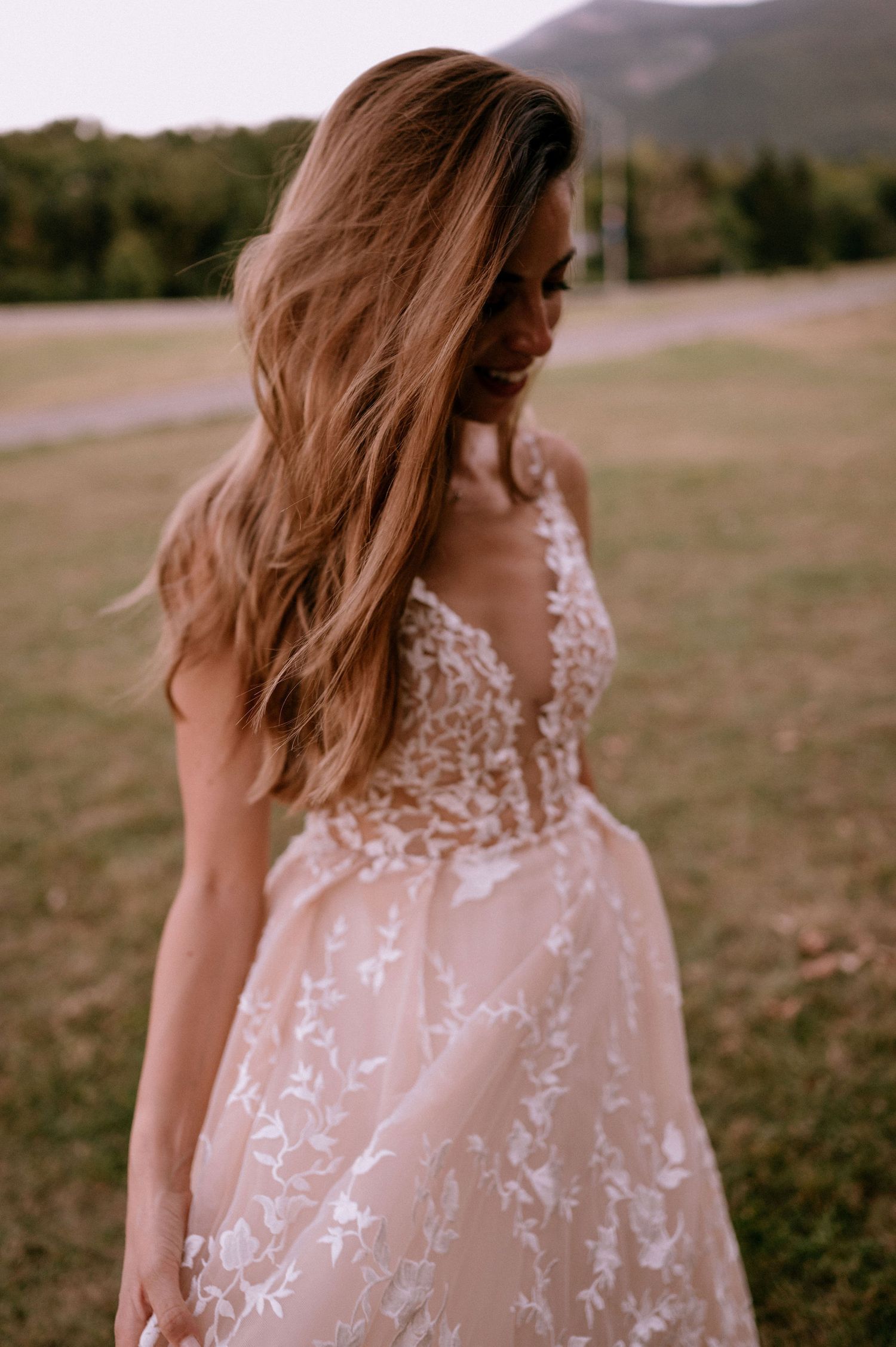 A delicate lace wedding dress with floral embroidery details shown in a field setting.