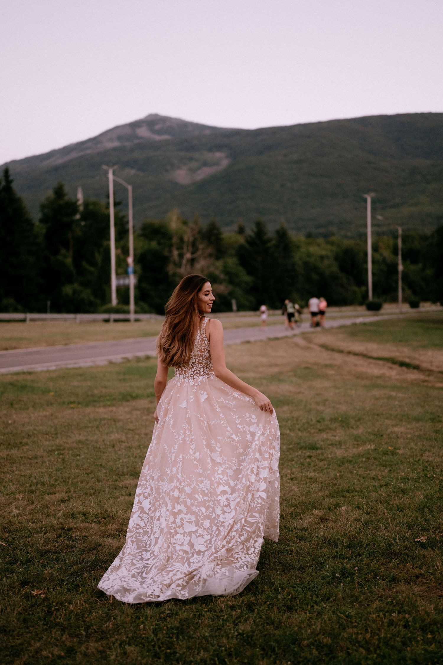 Elegant bride in blush lace gown poses against mountain landscape.