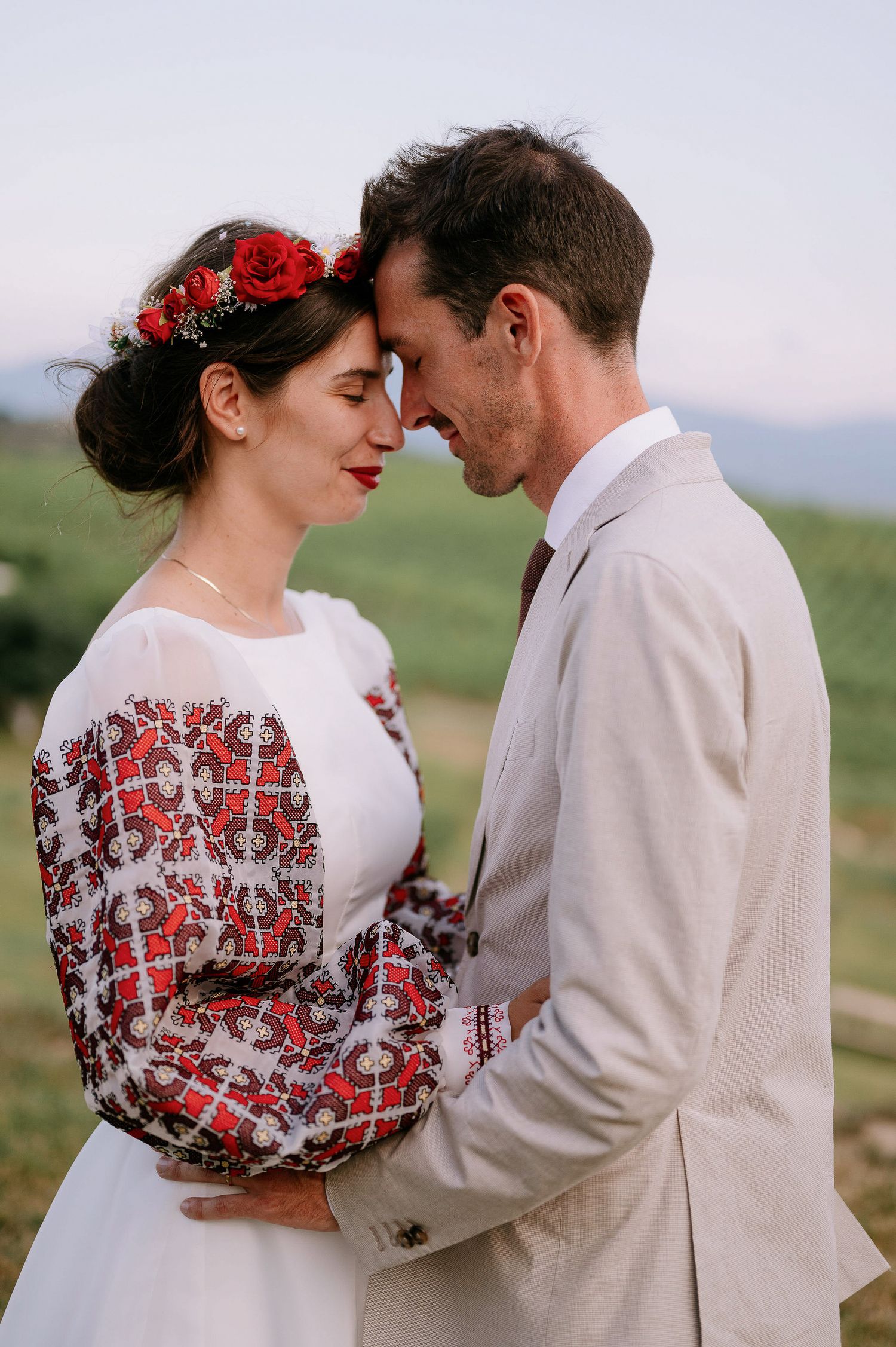 Intimate moment between newlyweds in traditional dress against mountain backdrop.
