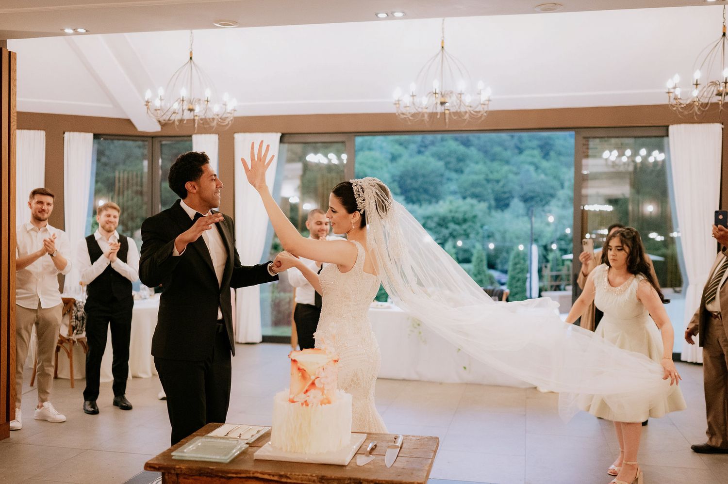 A couple celebrates during their wedding reception in an elegant room with chandeliers.