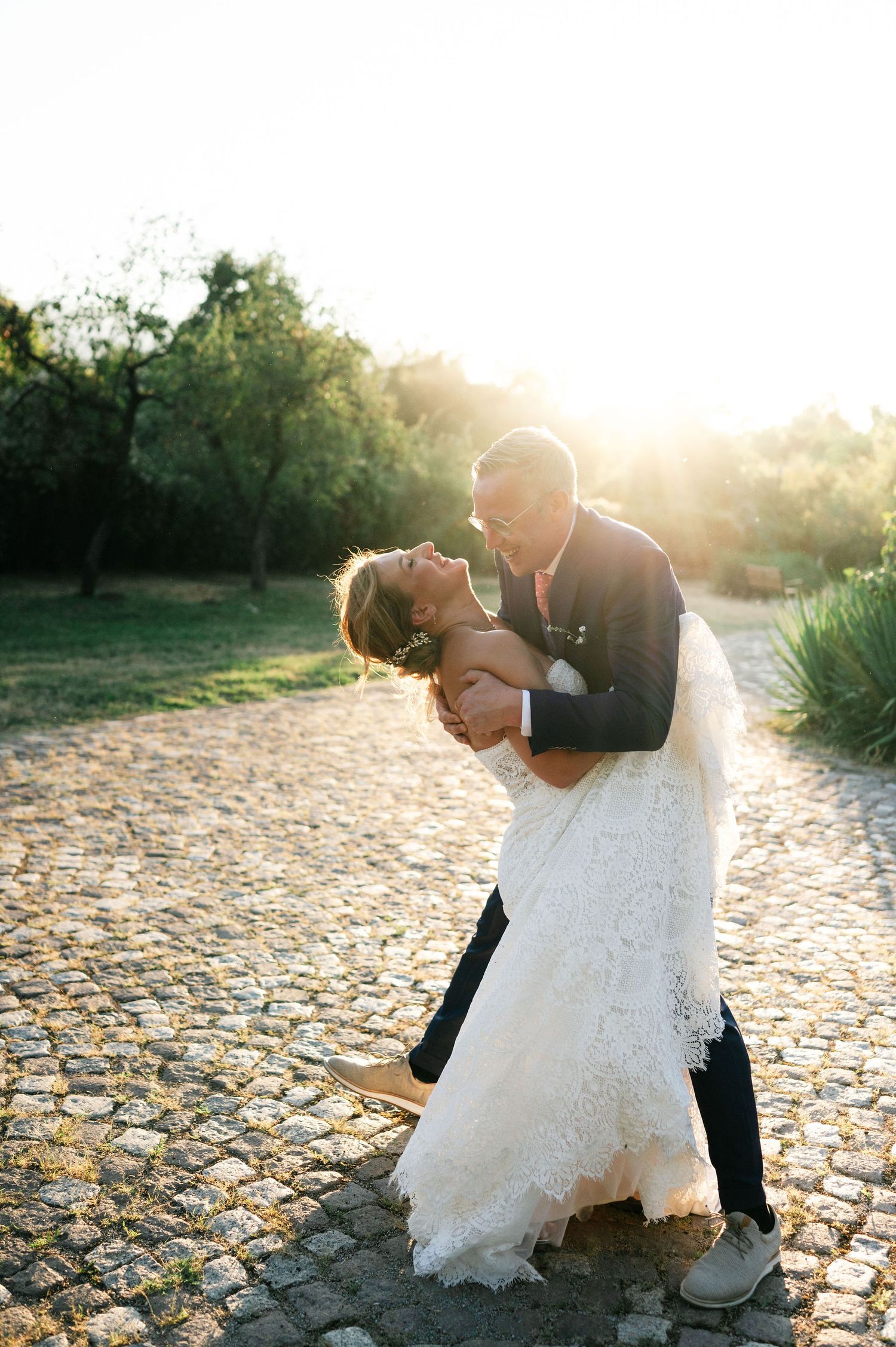 Dramatic wedding dip pose photographed during golden hour on stone pathway.