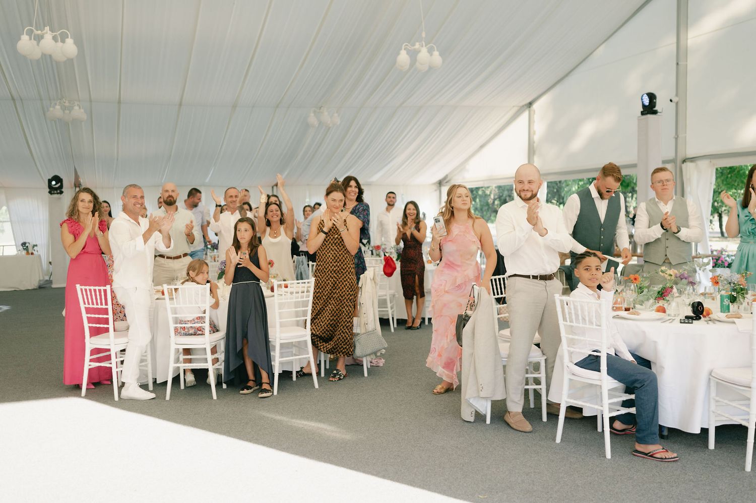 Wedding reception tent filled with guests seated at decorated round tables.