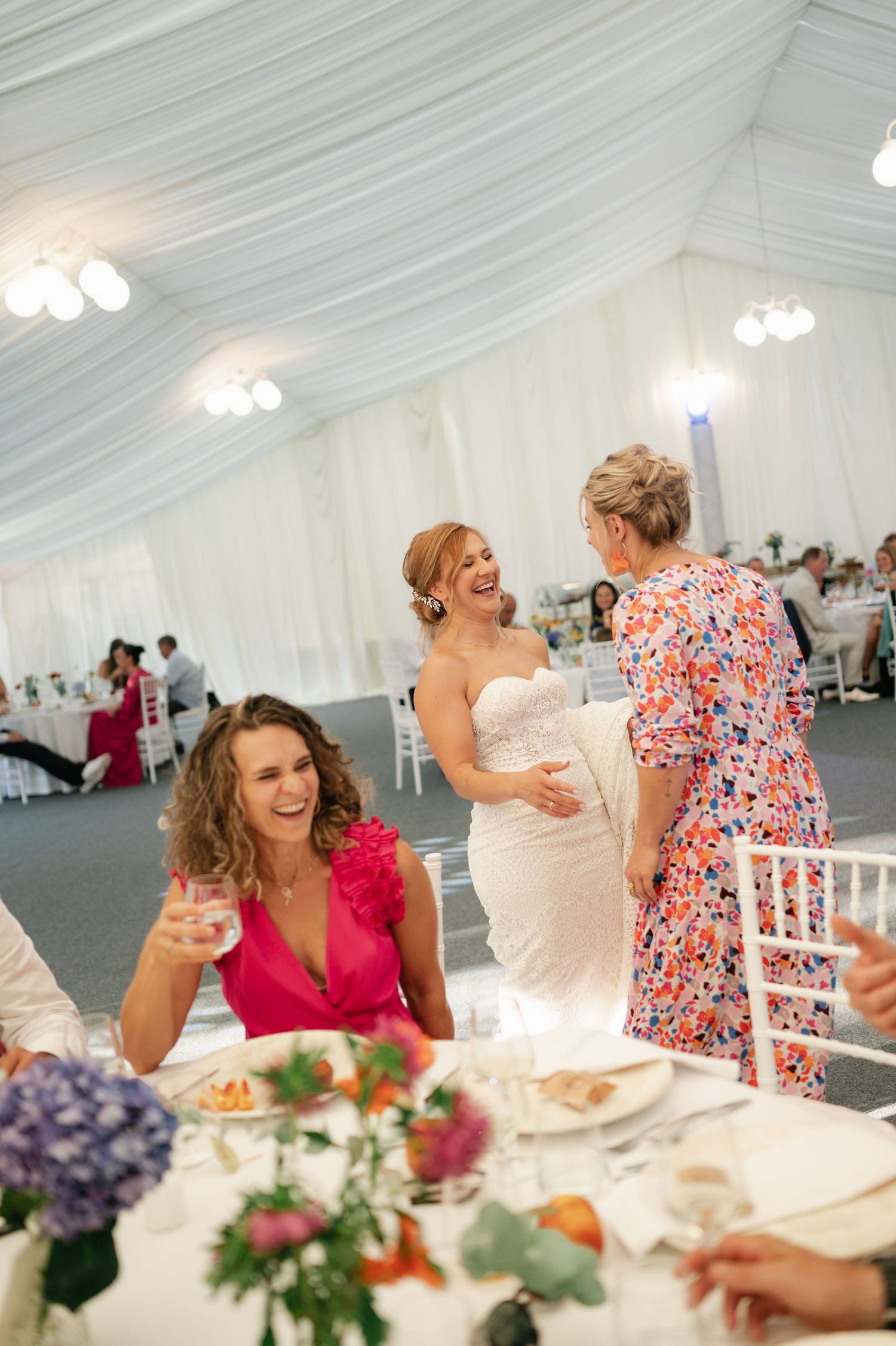 Wedding reception guests celebrating and raising glasses at decorated tables under white tent.
