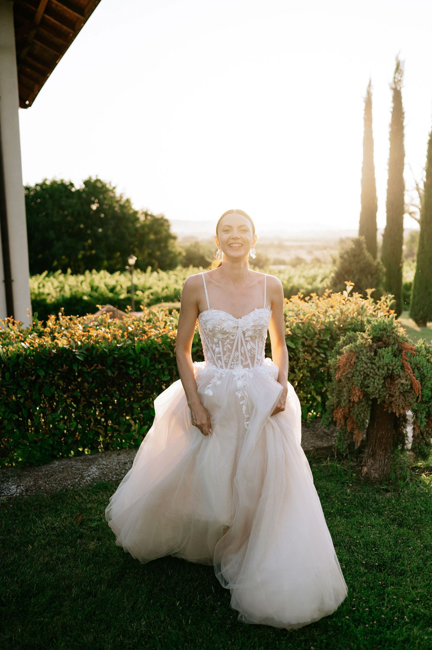 A wedding dress twirls in the late afternoon light against a backdrop of cypress trees and hedges.