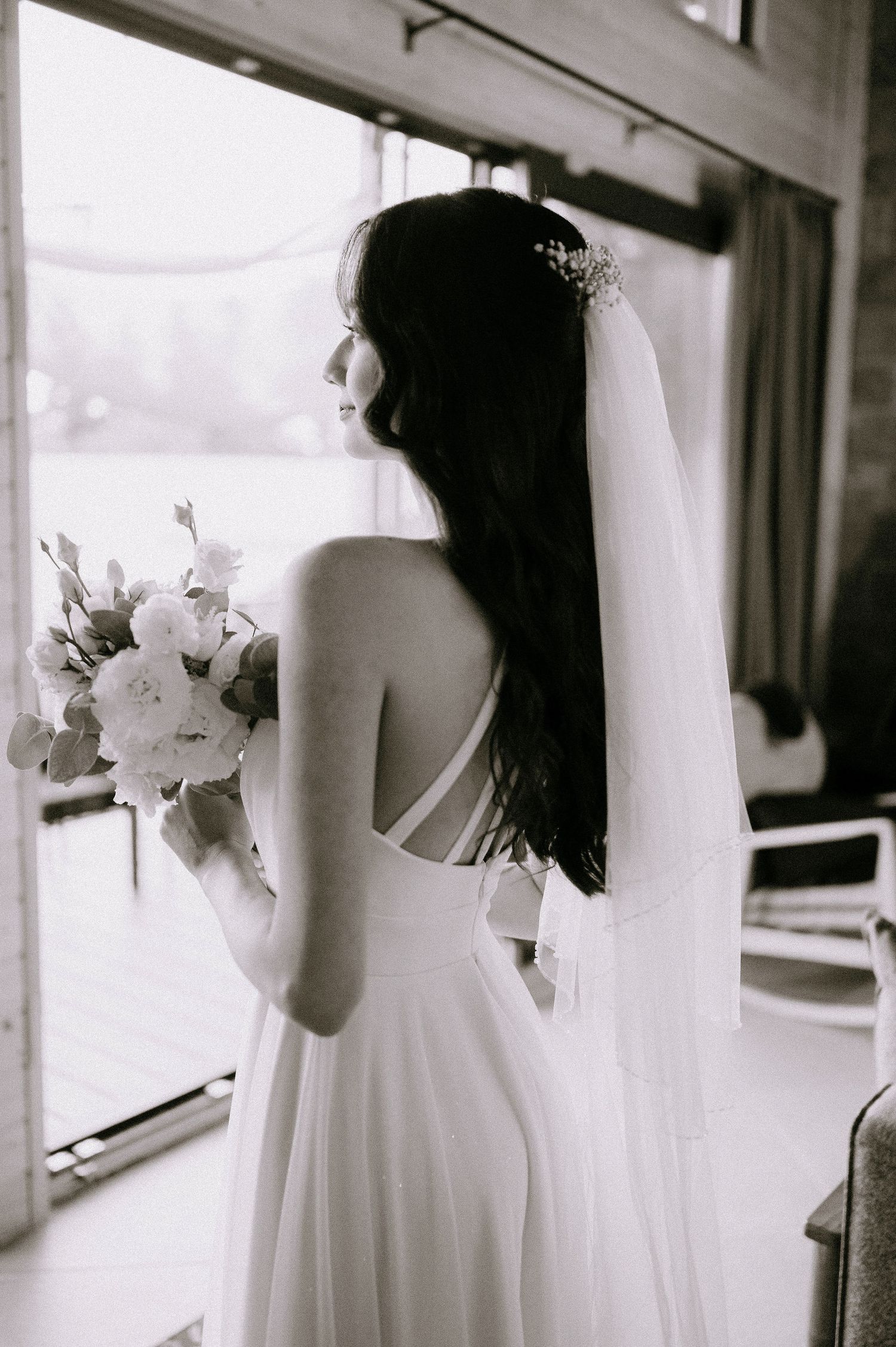 Black and white photos of bride with bouquet by large windows.