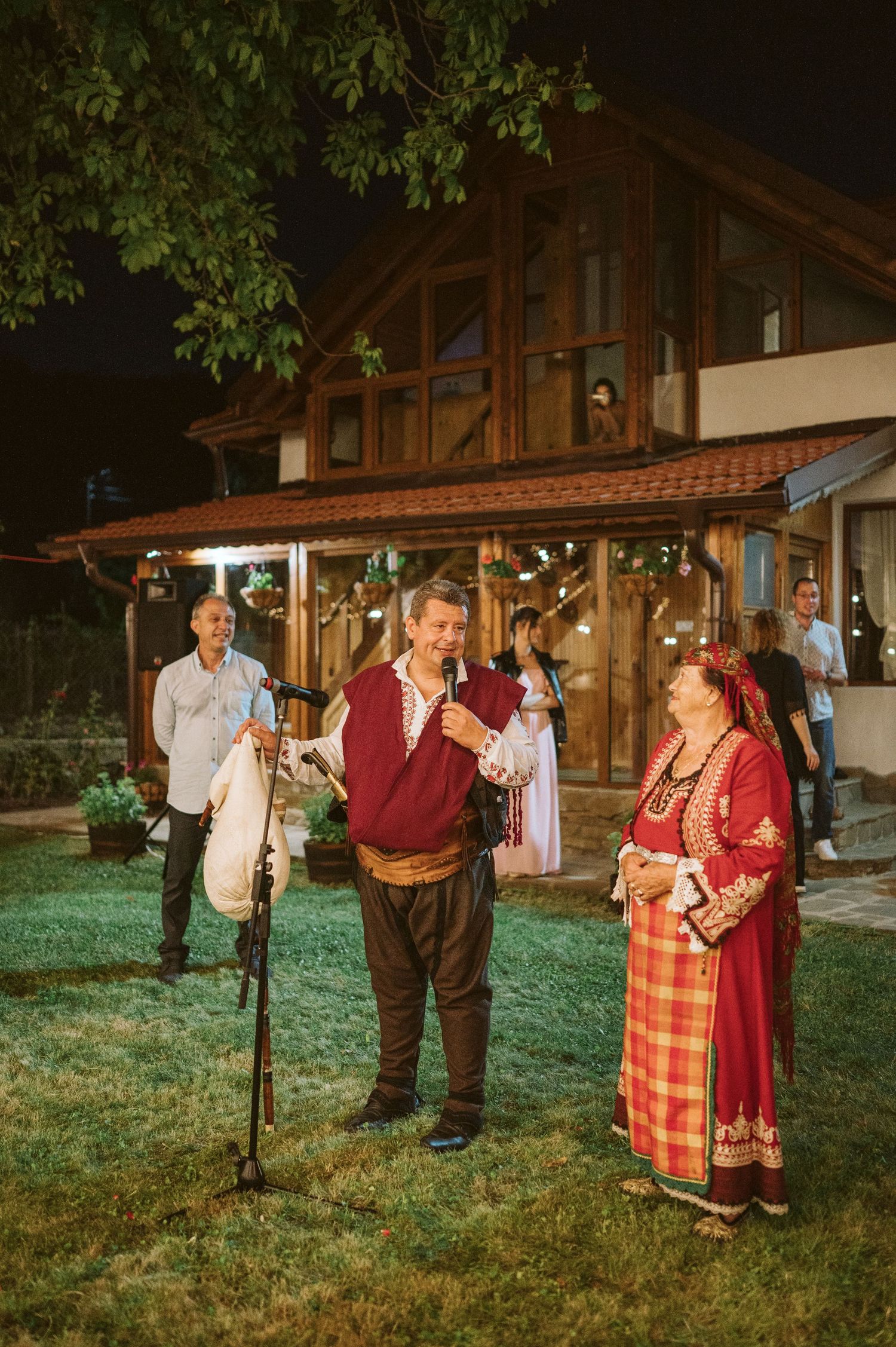 Traditional folk dancers in colorful costumes performing at an outdoor evening celebration.