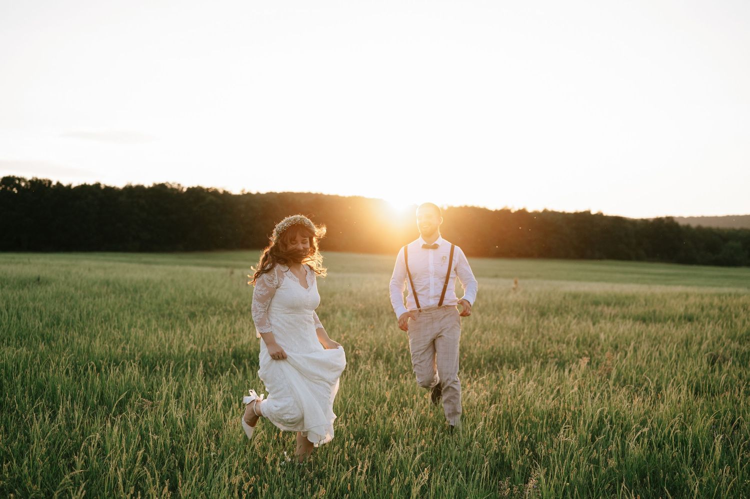 Couple walks through sunlit field during golden hour wedding photo session.