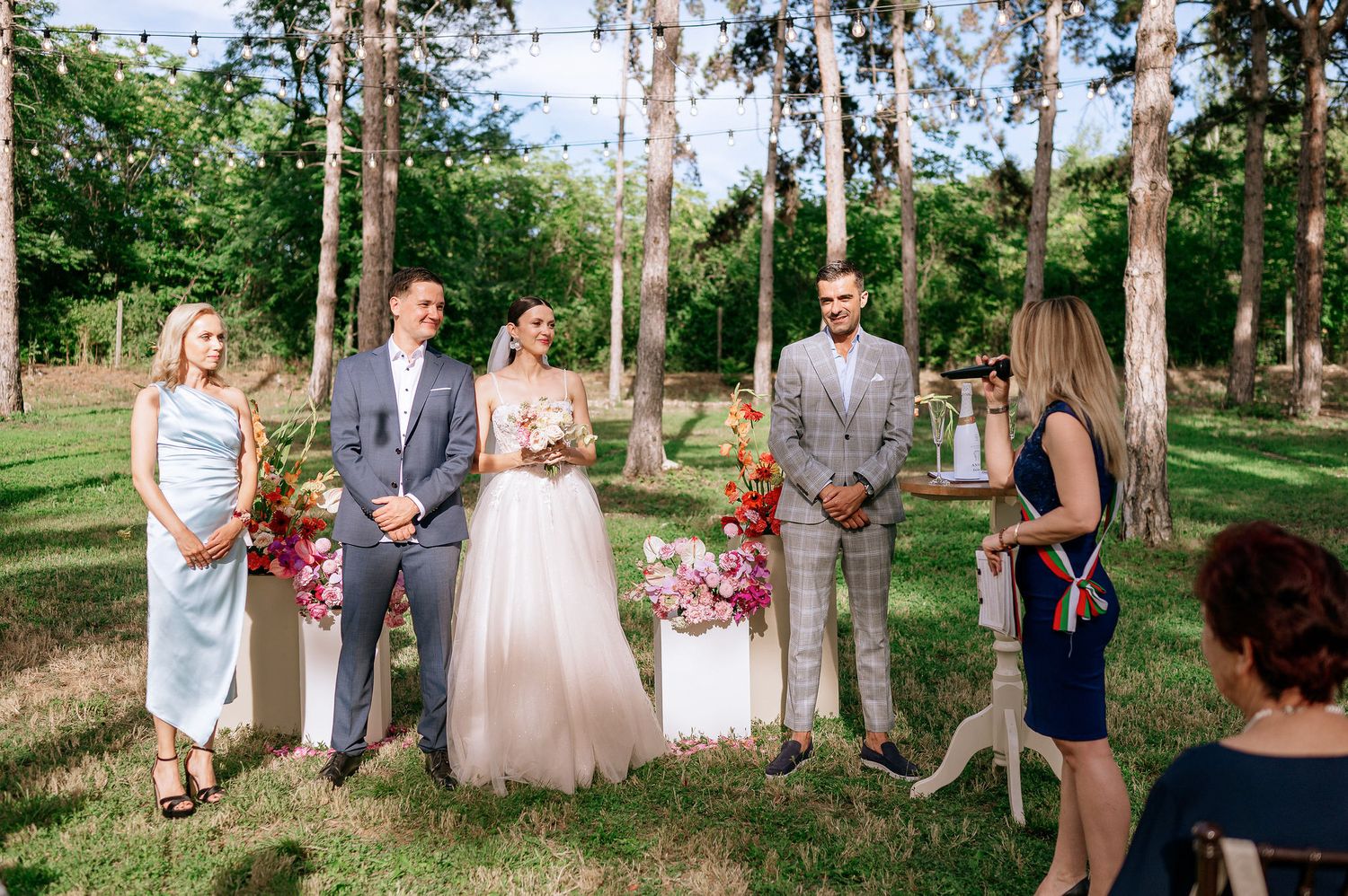 Wedding celebration with guests gathered in a natural forest setting with tall pine trees.