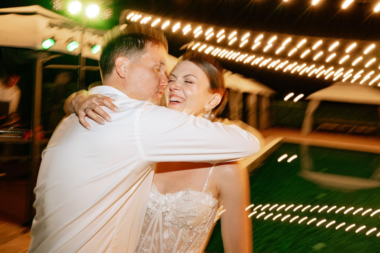Newlyweds embrace on the dance floor beneath warm string lights during their wedding celebration.