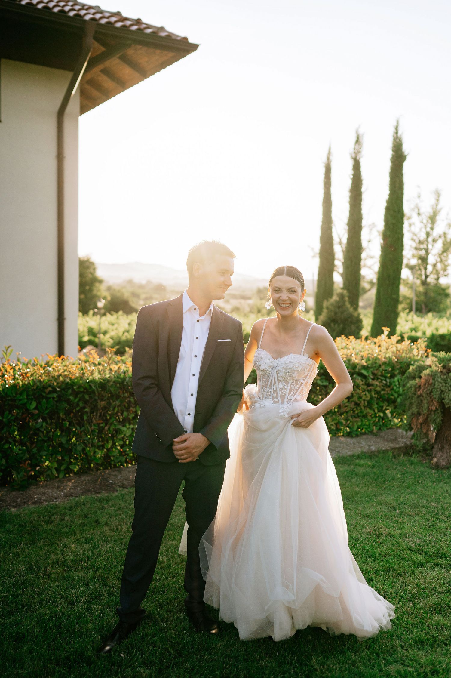 Couple sharing a romantic moment during sunset photoshoot in garden with cypress trees.