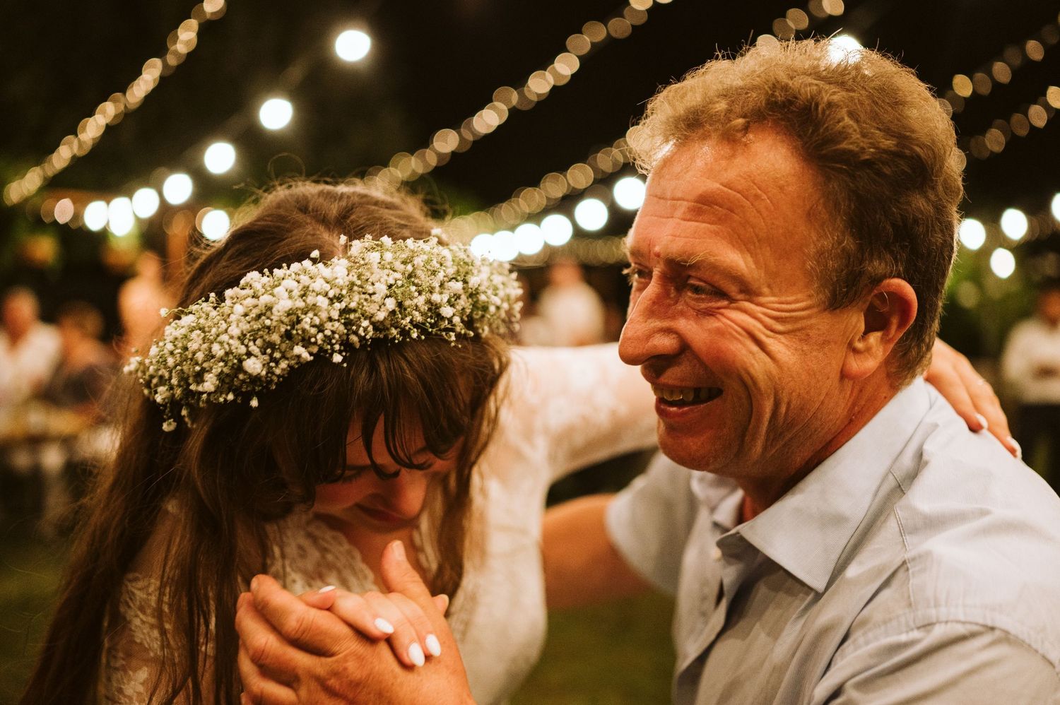 A couple shares a romantic dance moment under glowing string lights at their wedding reception.