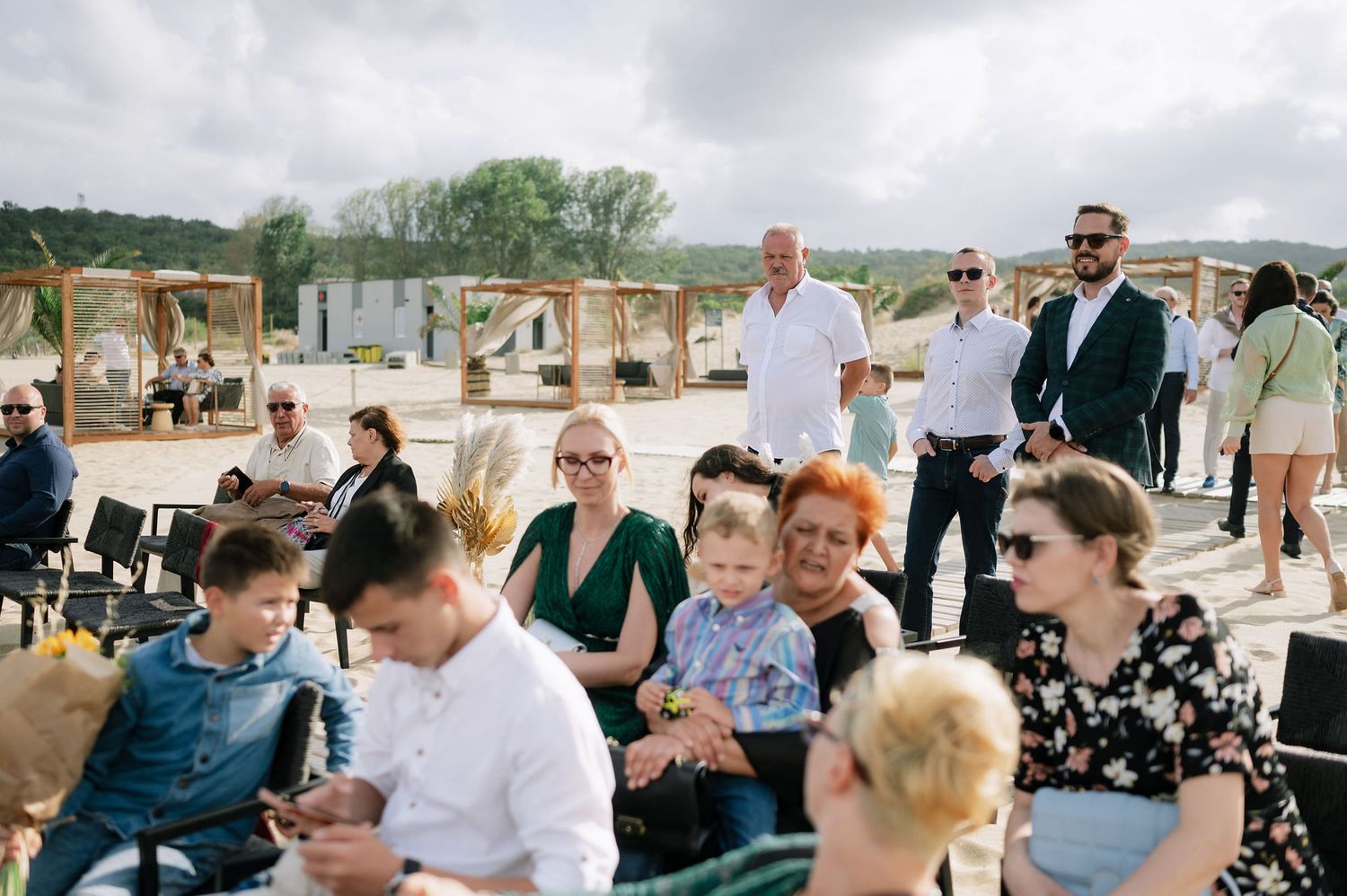 Casual outdoor gathering with guests seated on benches at a beachside venue.