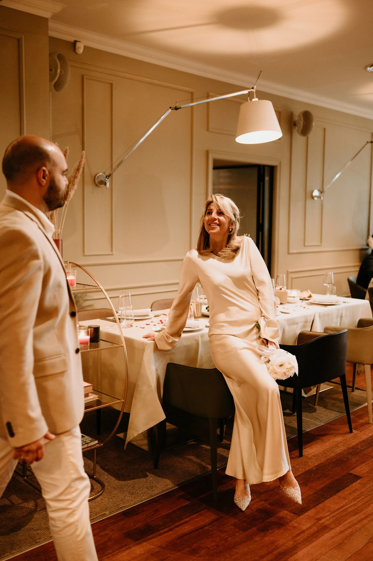 People in white attire dance and move across a wooden floor in an elegant indoor setting.