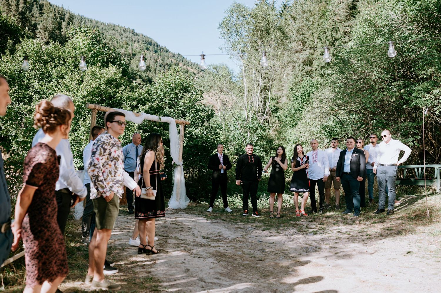 Panoramic view of wedding celebration outside historic stone building with mountain backdrop.