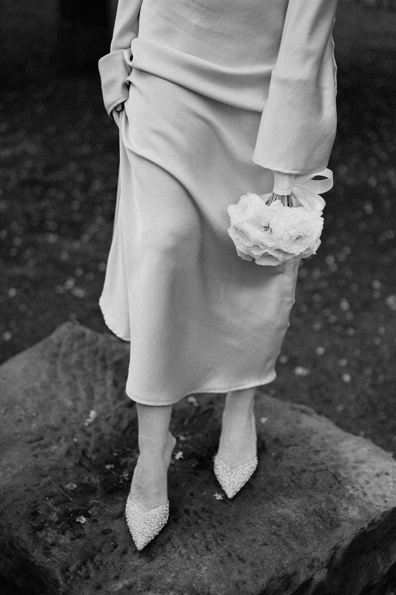 Elegant white bridal footwear and dress hem photographed in dramatic black and white.