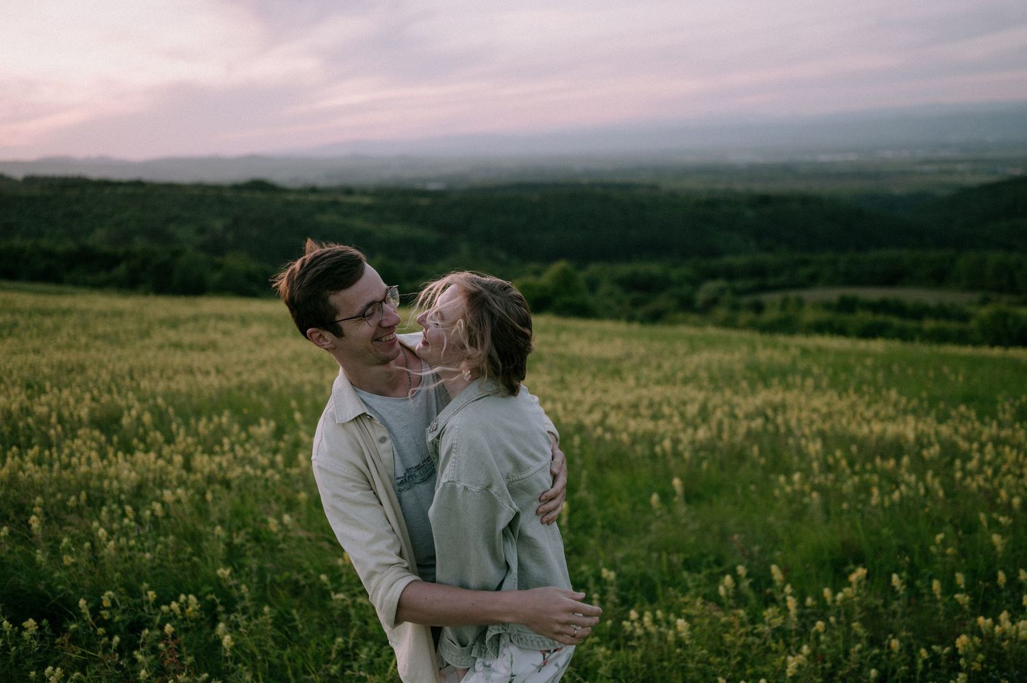 A couple embraces while dancing in a scenic mountain meadow at sunset.