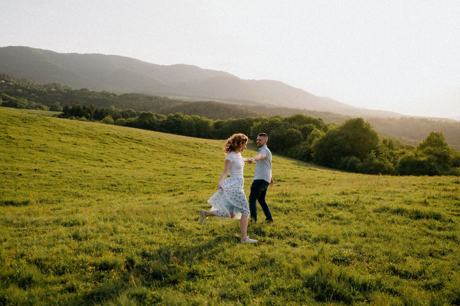Two figures dance and spin together on a scenic hilltop during sunset.