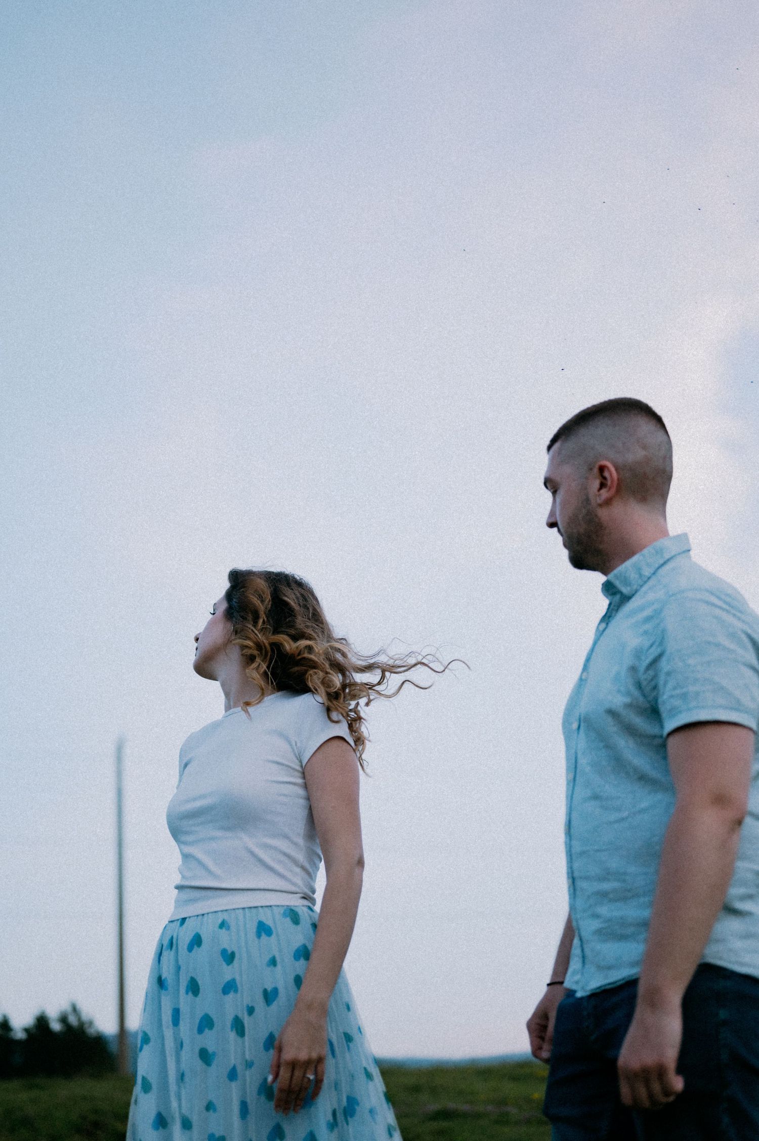 Two people walk together across a grassy field during a moody evening photoshoot.