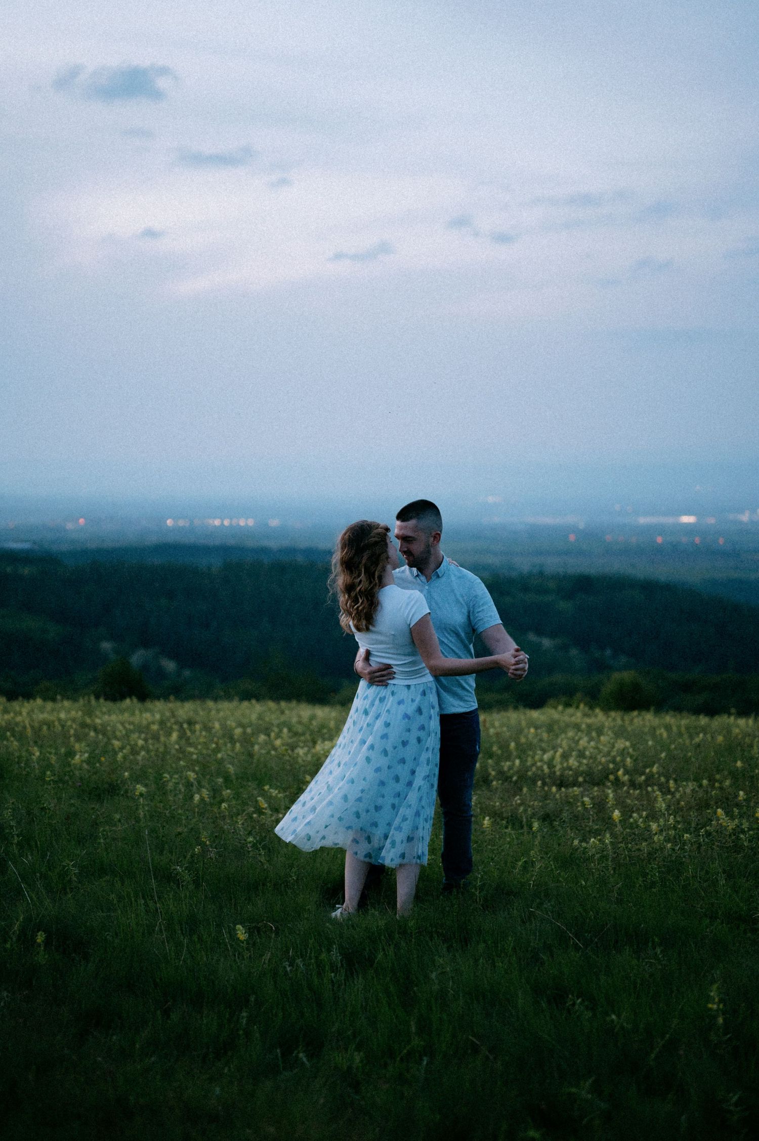 Two people dancing together in a wildflower field at dusk.