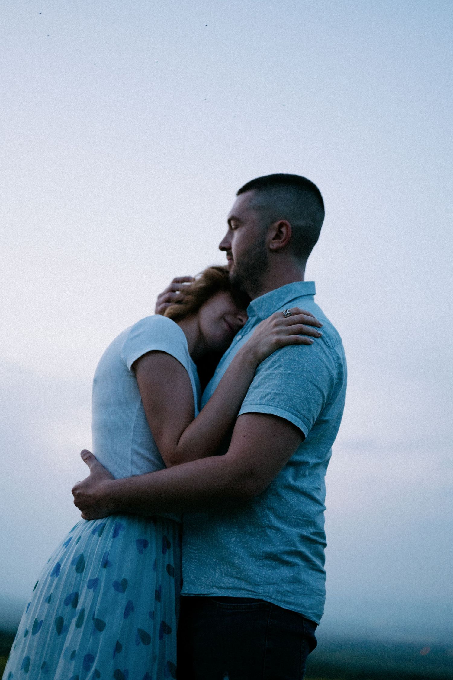 A romantic embrace between two people on a hilltop during sunset.