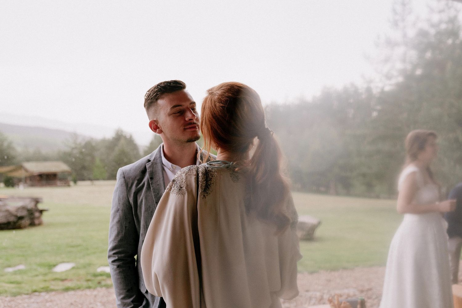 Intimate moment captured at an outdoor wedding with misty mountains in the background.