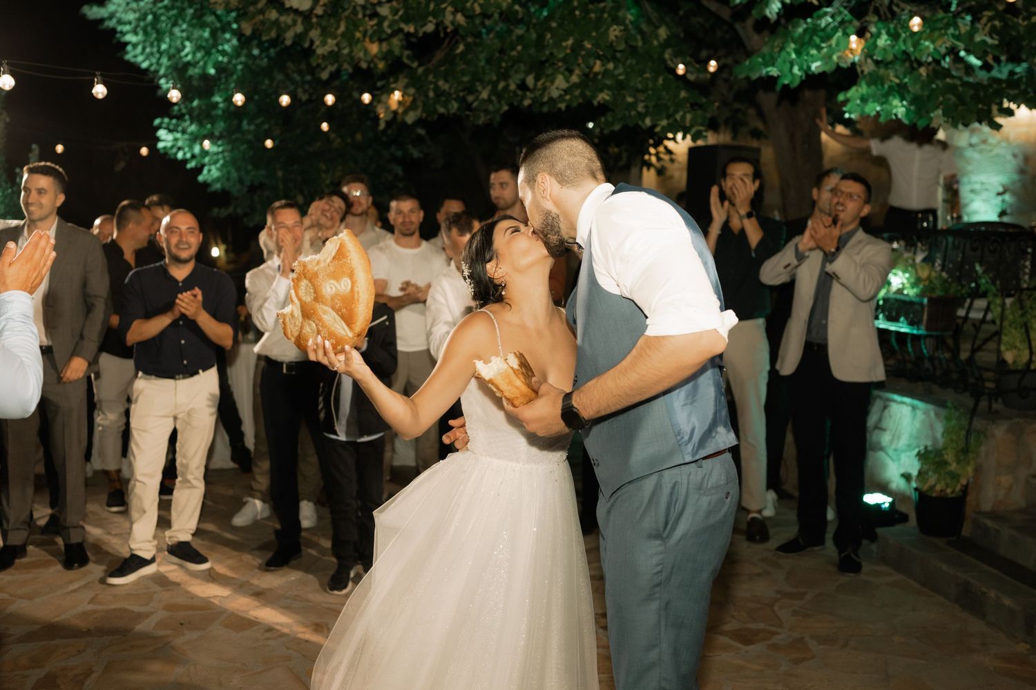 A couple shares their first dance at an outdoor evening wedding reception while guests watch and celebrate.