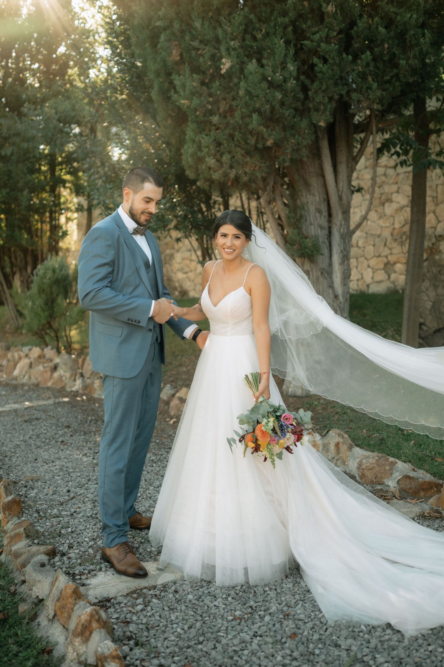 A couple in wedding attire poses on a gravel path while a golden retriever dog sits nearby during their outdoor photoshoot.