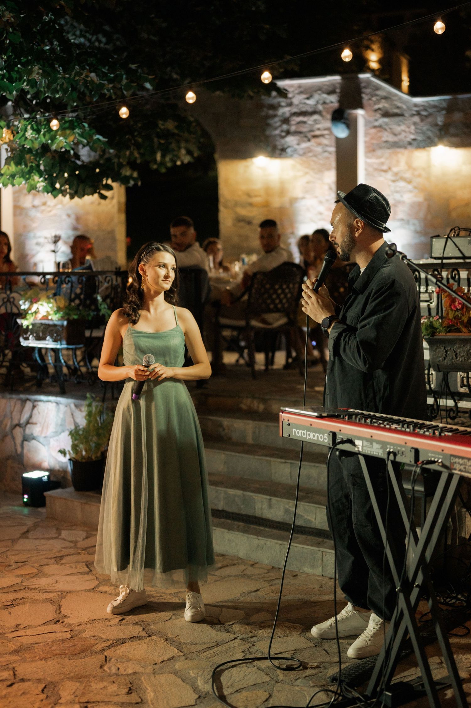 A couple performs a romantic dance together at an outdoor stone patio venue illuminated by string lights.