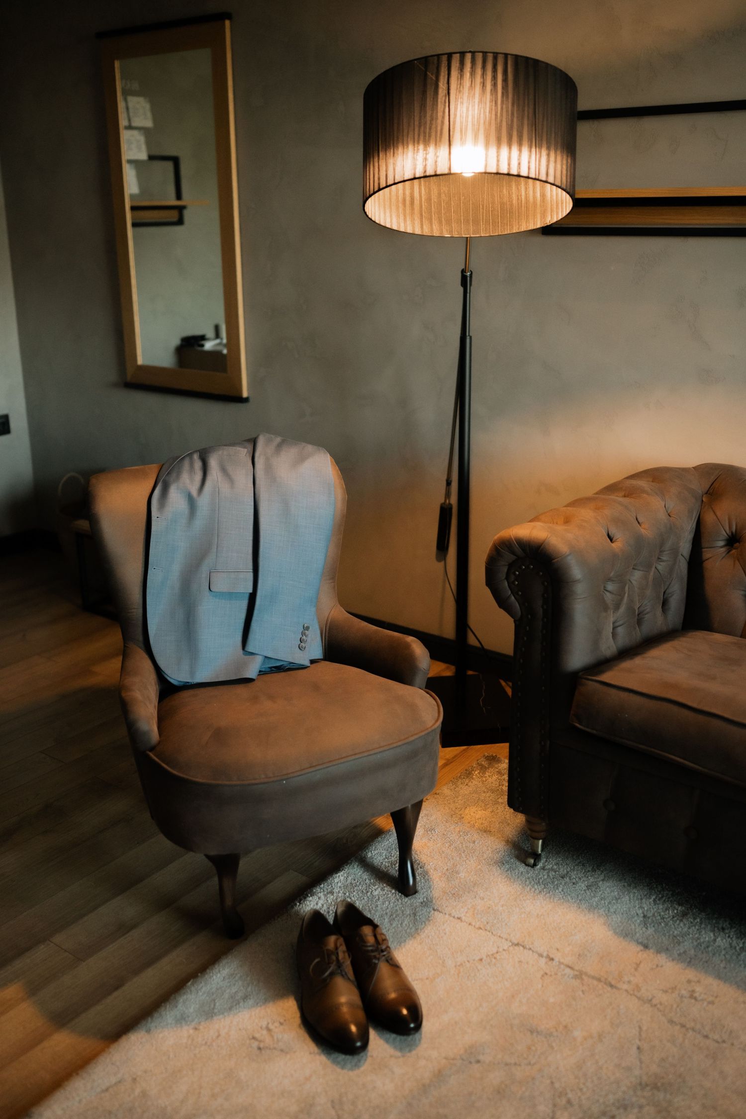 A series of dark moody photos showing a leather couch with brown leather shoes placed underneath in dim lighting.