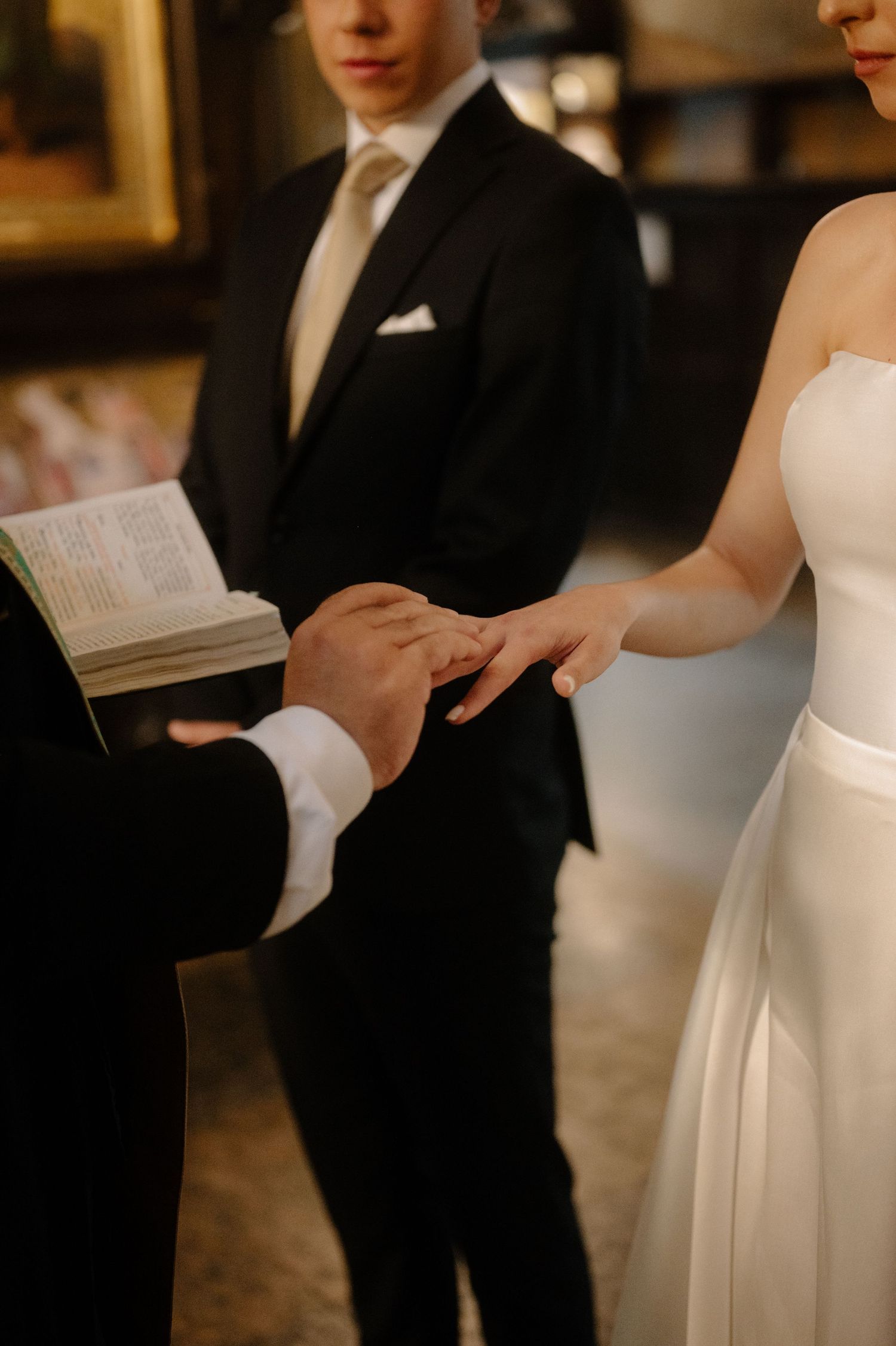 Close-up of hands during wedding ceremony as couple exchanges rings with officiant and groom in background.