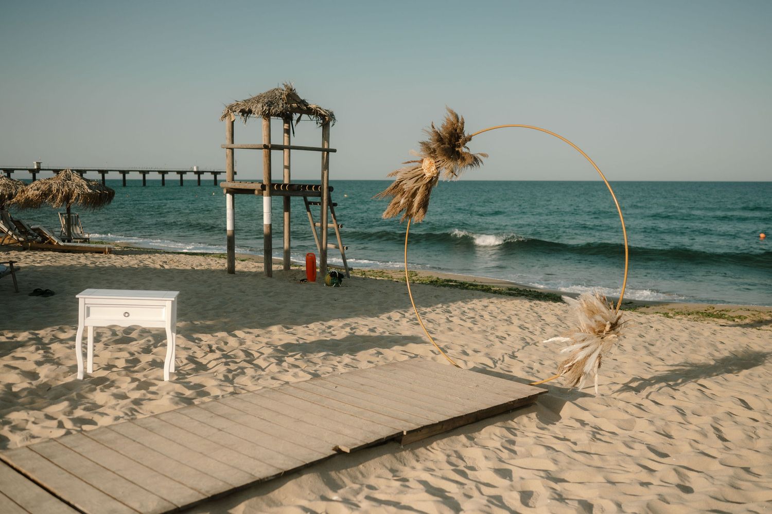 A wooden boardwalk leads to a tropical beach with palm trees and turquoise ocean waters under a sunny sky.