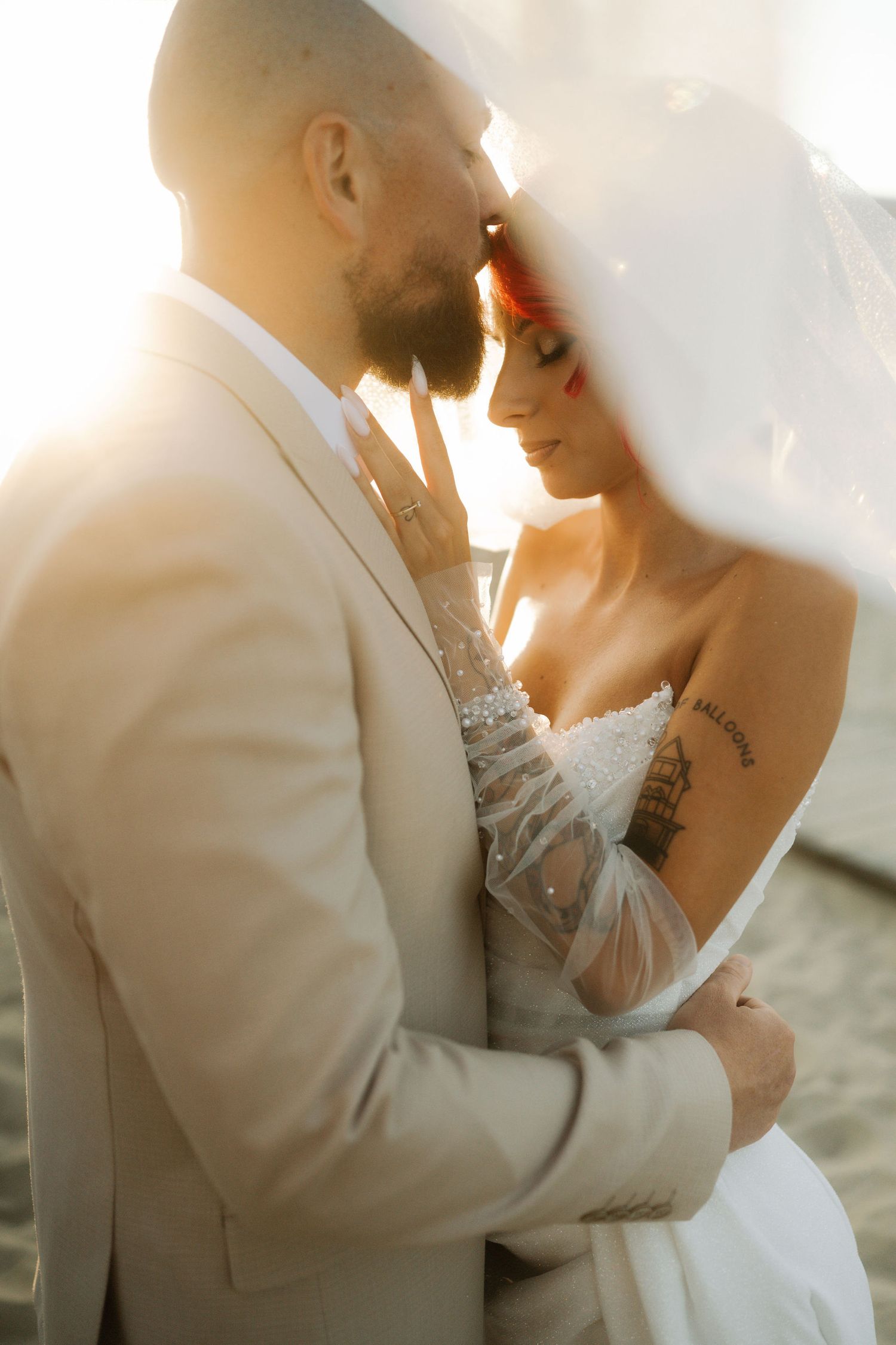 Intimate wedding portrait of couple in warm sunlight with bride in white dress and groom in light suit.