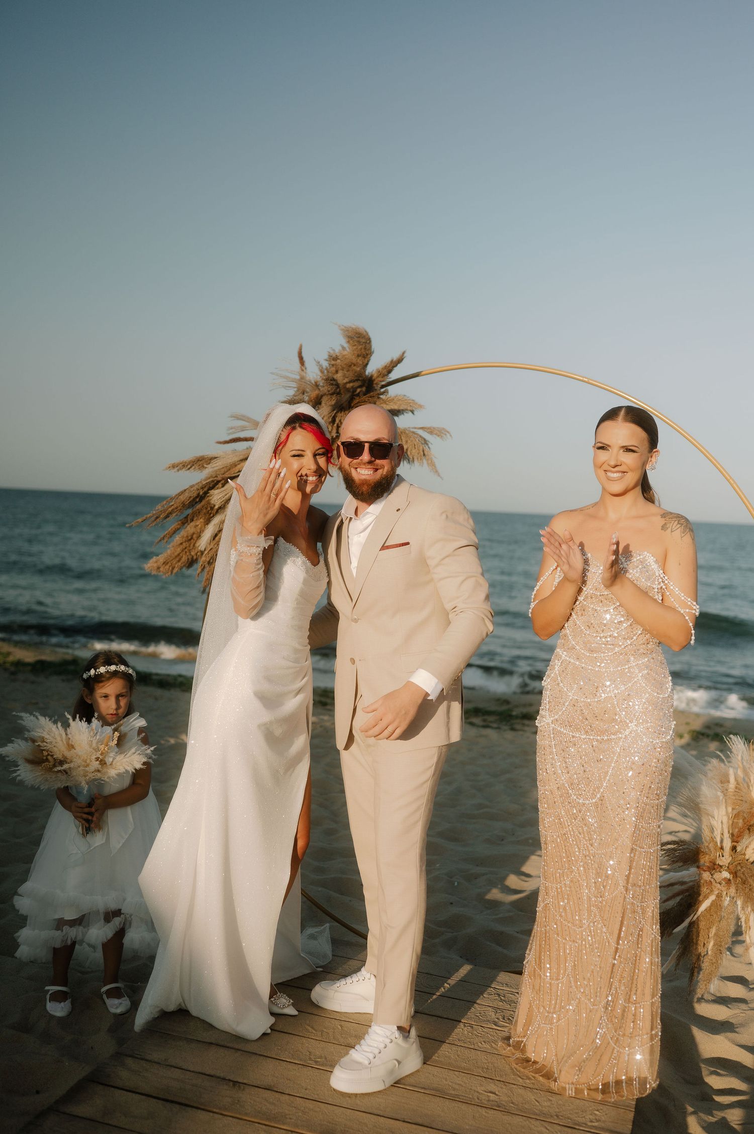 Wedding party poses together on wooden deck by ocean at sunset with pampas grass decorations and beachy vibes.