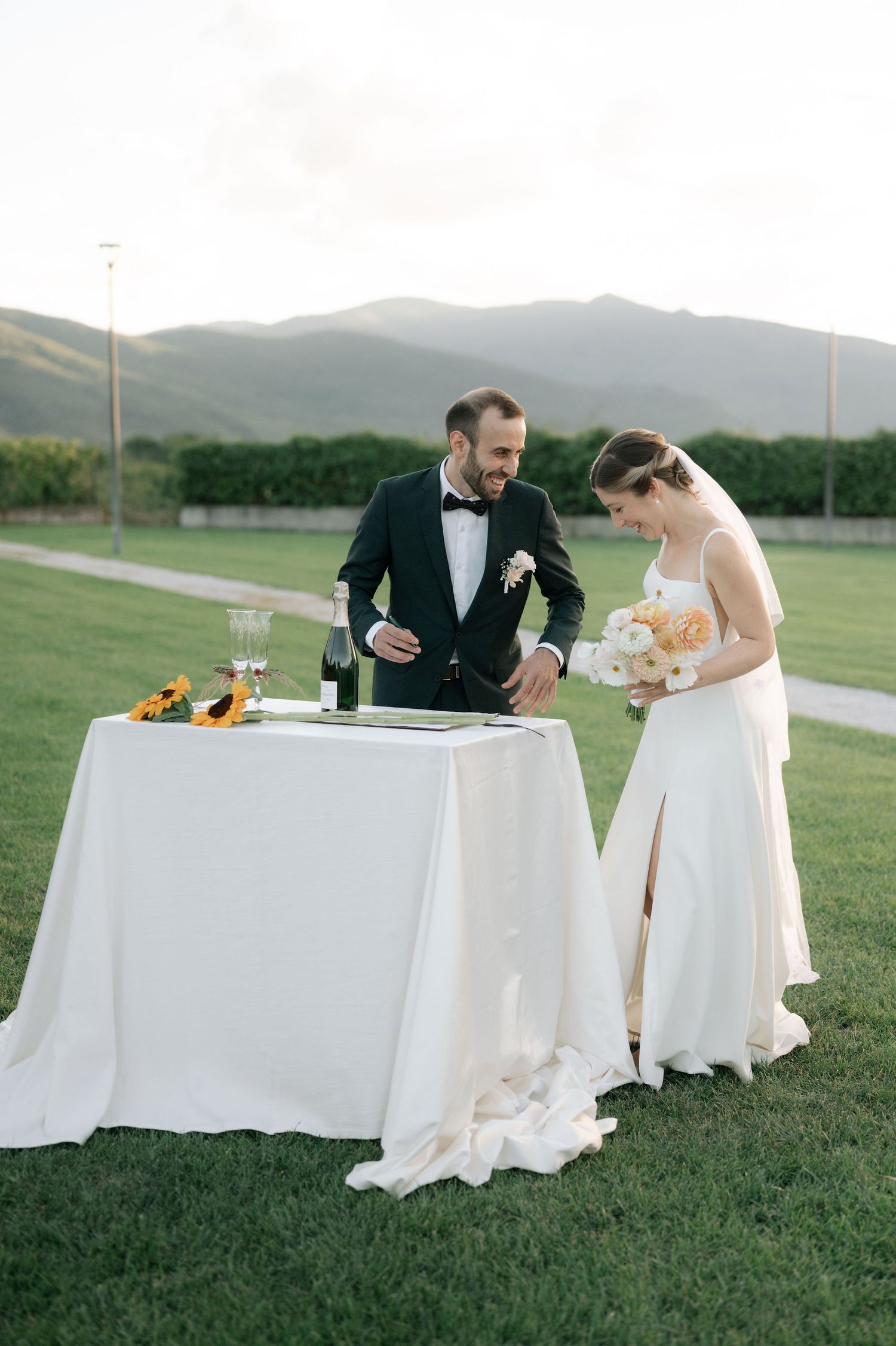 Elegant outdoor wedding reception with couple at white-clothed table featuring sunflower decor and mountain views.