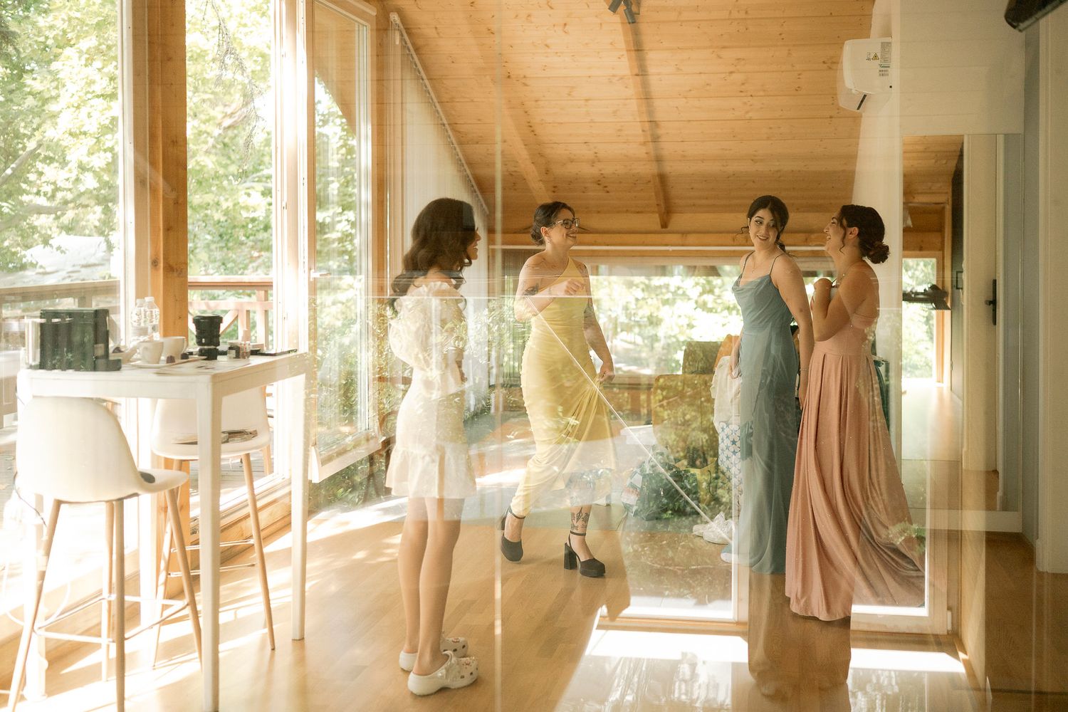 Ballet dancers practice at wooden barre in sunlit studio with large windows and hardwood floors.